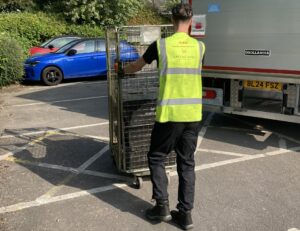 Member of GXO staff wearing GXO high vis top pushing a trolley to the back of a lorry